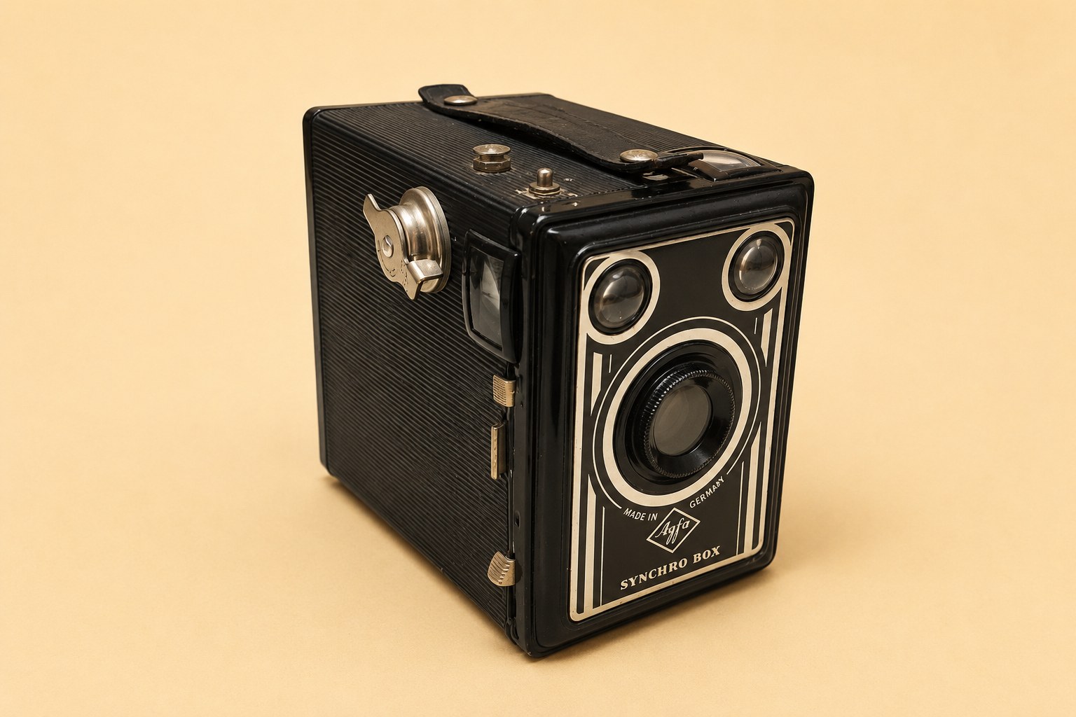 A black Agfa Synchro-Box box camera, Made in Germany, with two brilliant finders and a central lens; shown with its back open, its embossed metal body, a Fujifilm Provia 400F 120 film spool marked 'EXPOSED', and the complete folded multilingual Agfa Synchro-Box instruction leaflet.