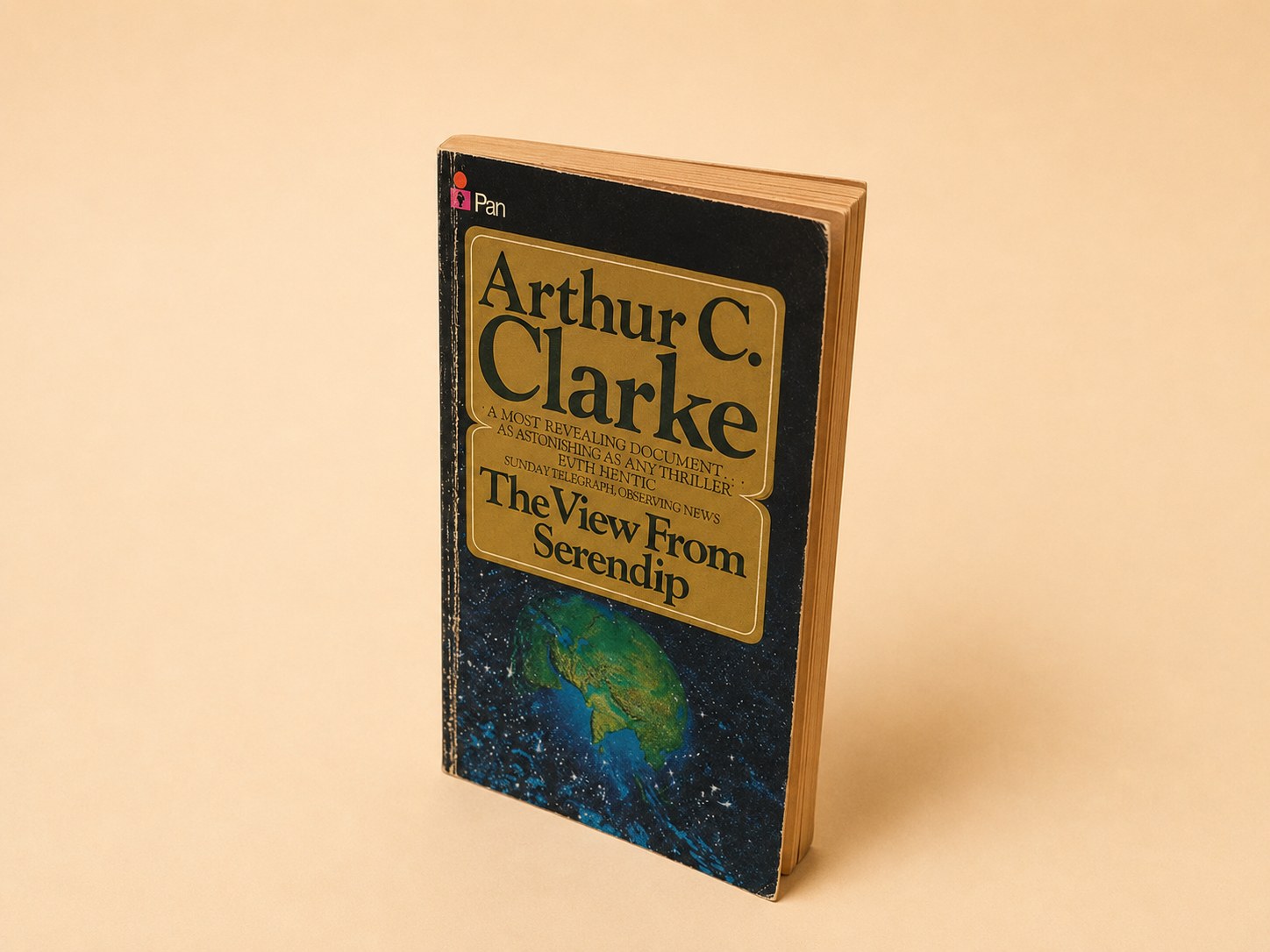 A 1979 Pan paperback of Arthur C. Clarke's 'The View from Serendip', shown spine and front cover with a globe motif, and opened to the title page bearing a handwritten ink inscription 'To Professor Shoenberg, with all good wishes, Arthur C. Clarke, Colombo, 1980'.